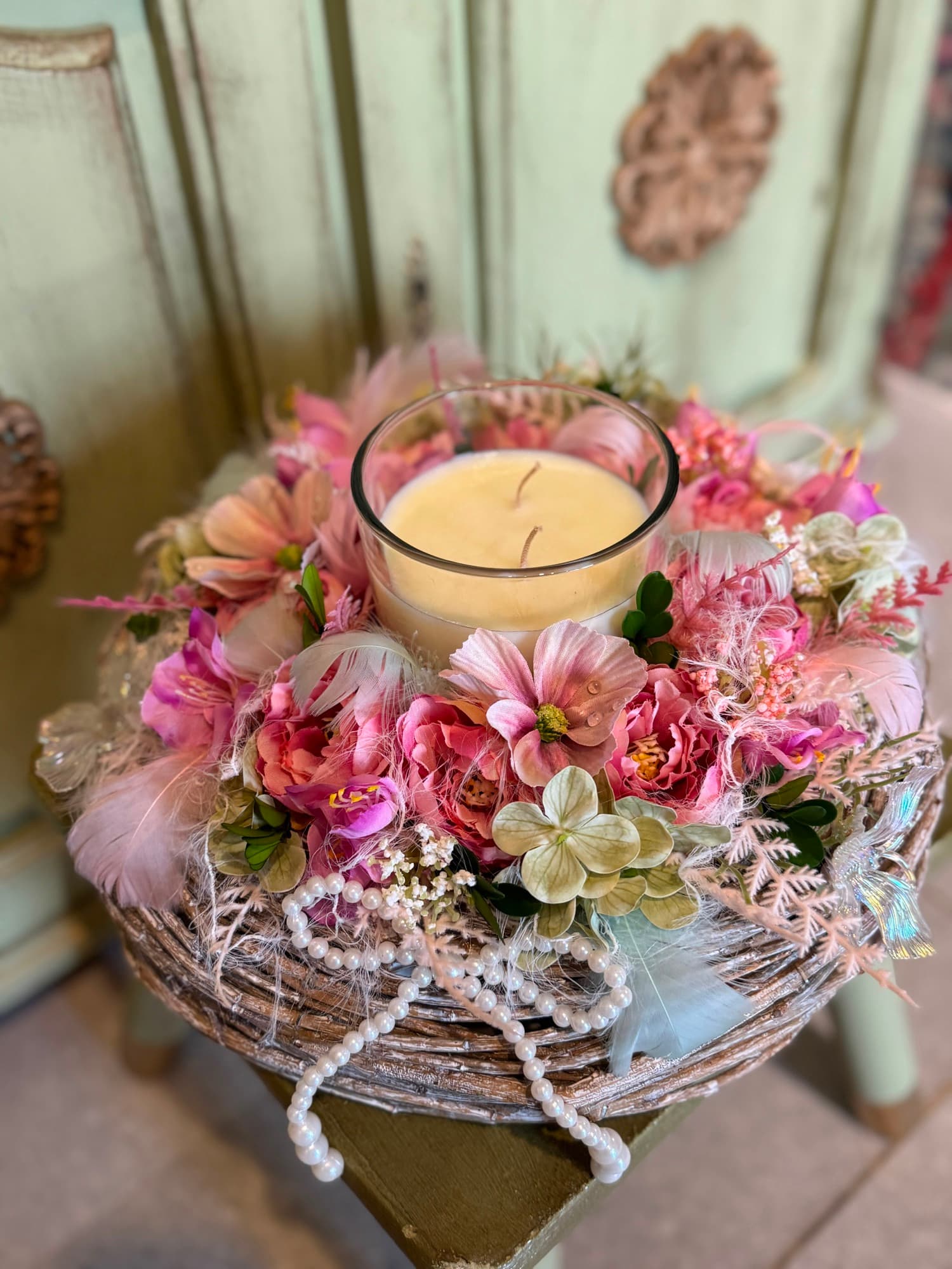 A small wreath with a candle and pink flowers in a basket